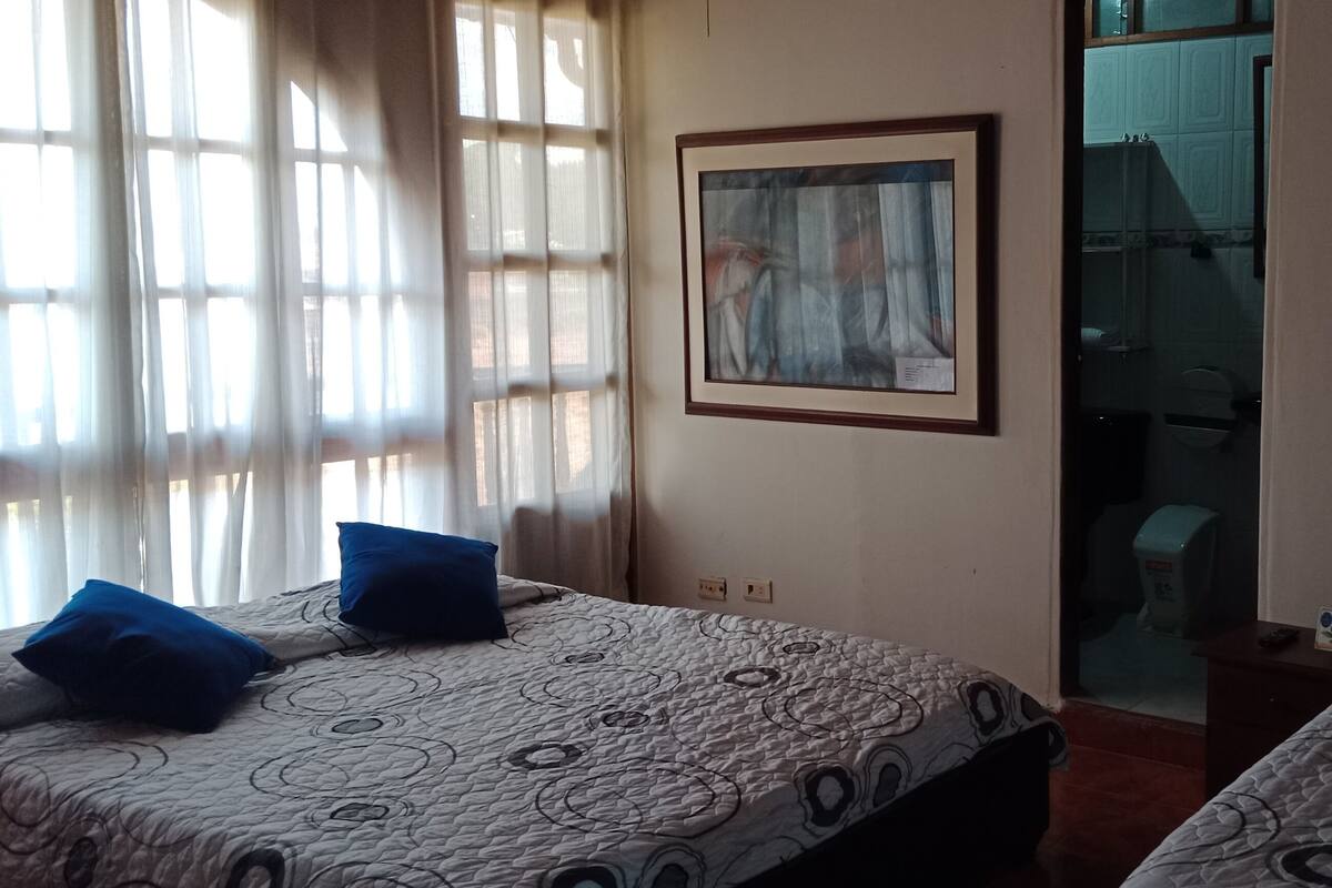 A hotel room with two beds, a framed abstract painting, and a bathroom visible through a glass door.