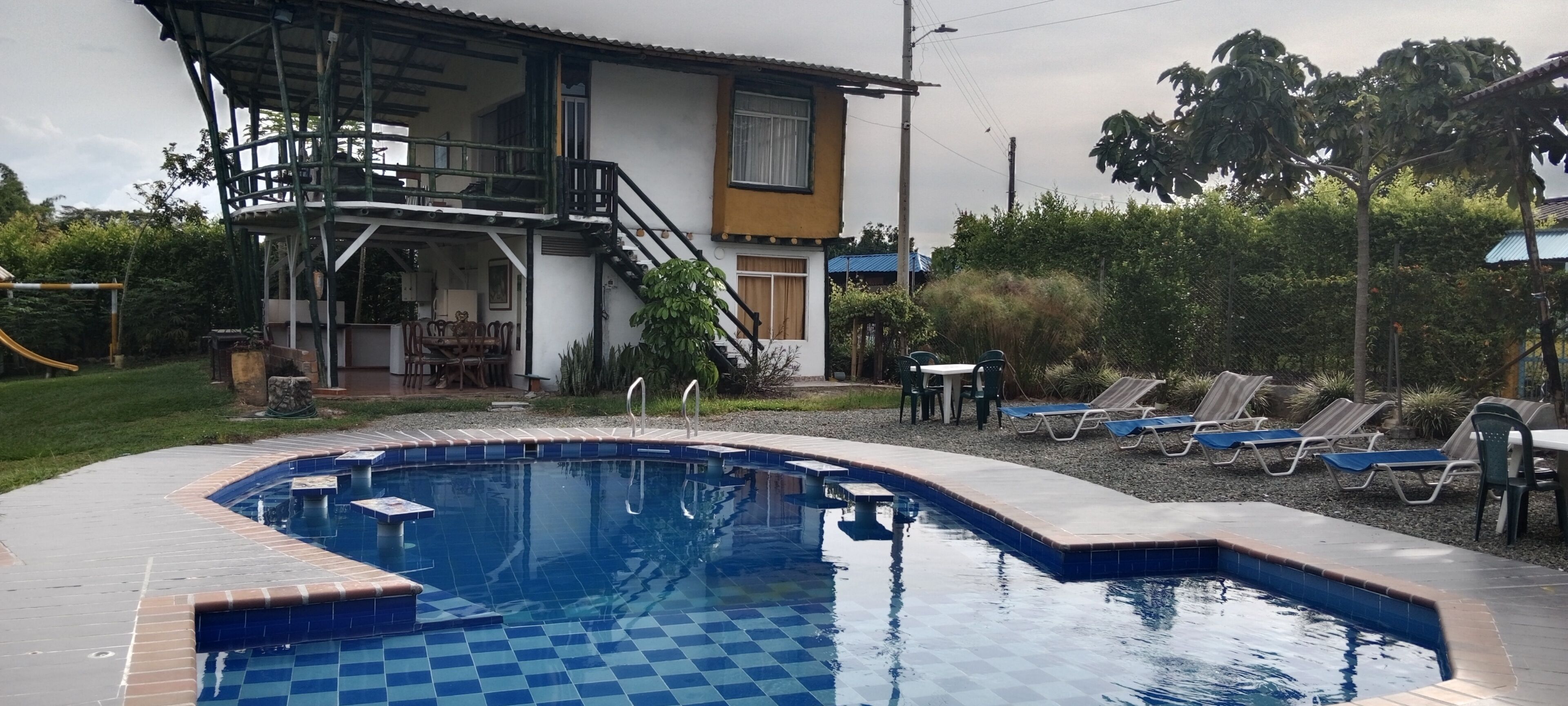 A swimming pool with a checkered pattern, surrounded by lounge chairs and a covered seating area.