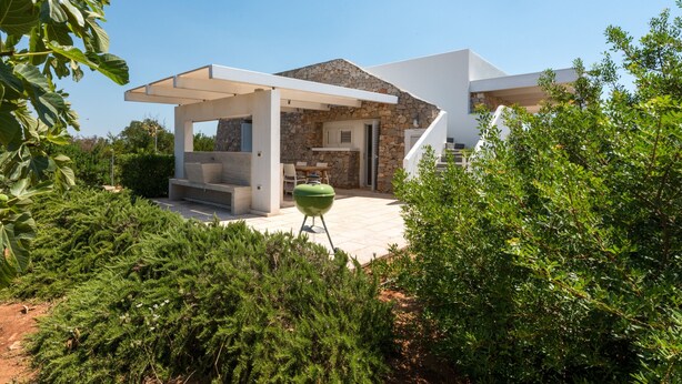 A modern house with a stone facade, a covered patio, and a green lawn.
