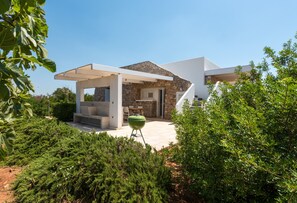 Une maison moderne avec une façade en pierre, un patio couvert et une pelouse verdoyante.