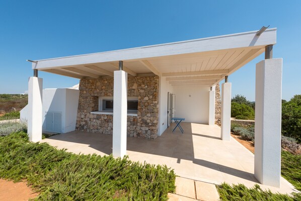 Une terrasse extérieure moderne, agrémentée d’un mur en pierre, d’un barbecue encastré et d’une table pliante bleue.