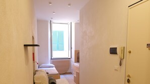 A narrow hallway with a bed, a white door, and a window with shutters. - Casa Vittoria by PortofinoVacanze (Rapallo)