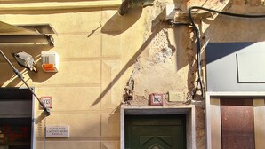 A green door with a metal handle, a sign above it, and a building facade with a textured wall and a window displaying a mannequin. - Casa Vittoria by PortofinoVacanze (Rapallo)