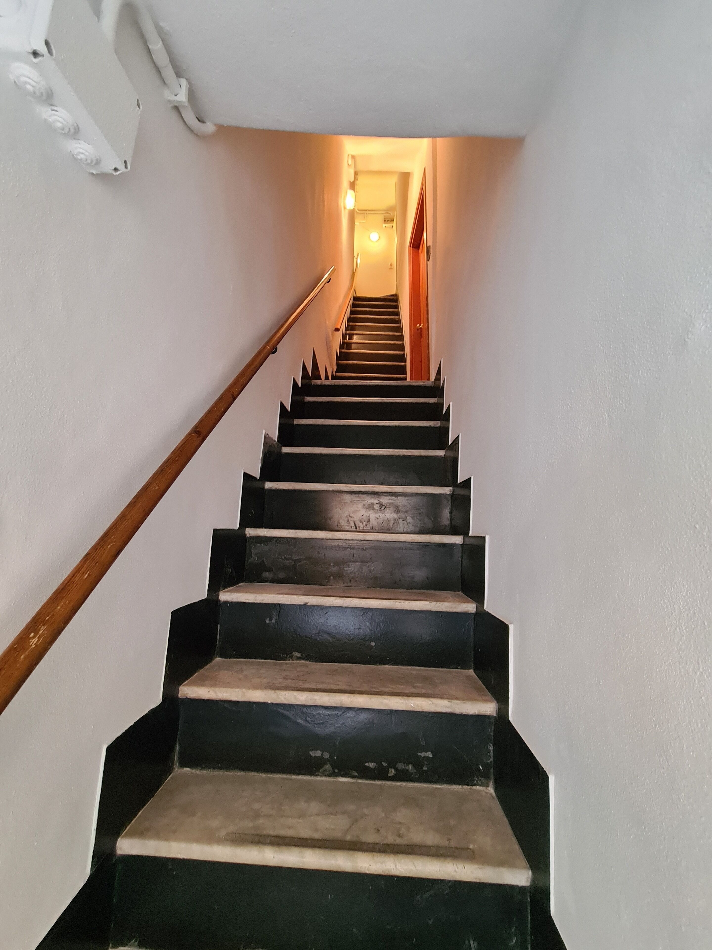 A staircase with wooden handrails and black steps leading to a door at the top.