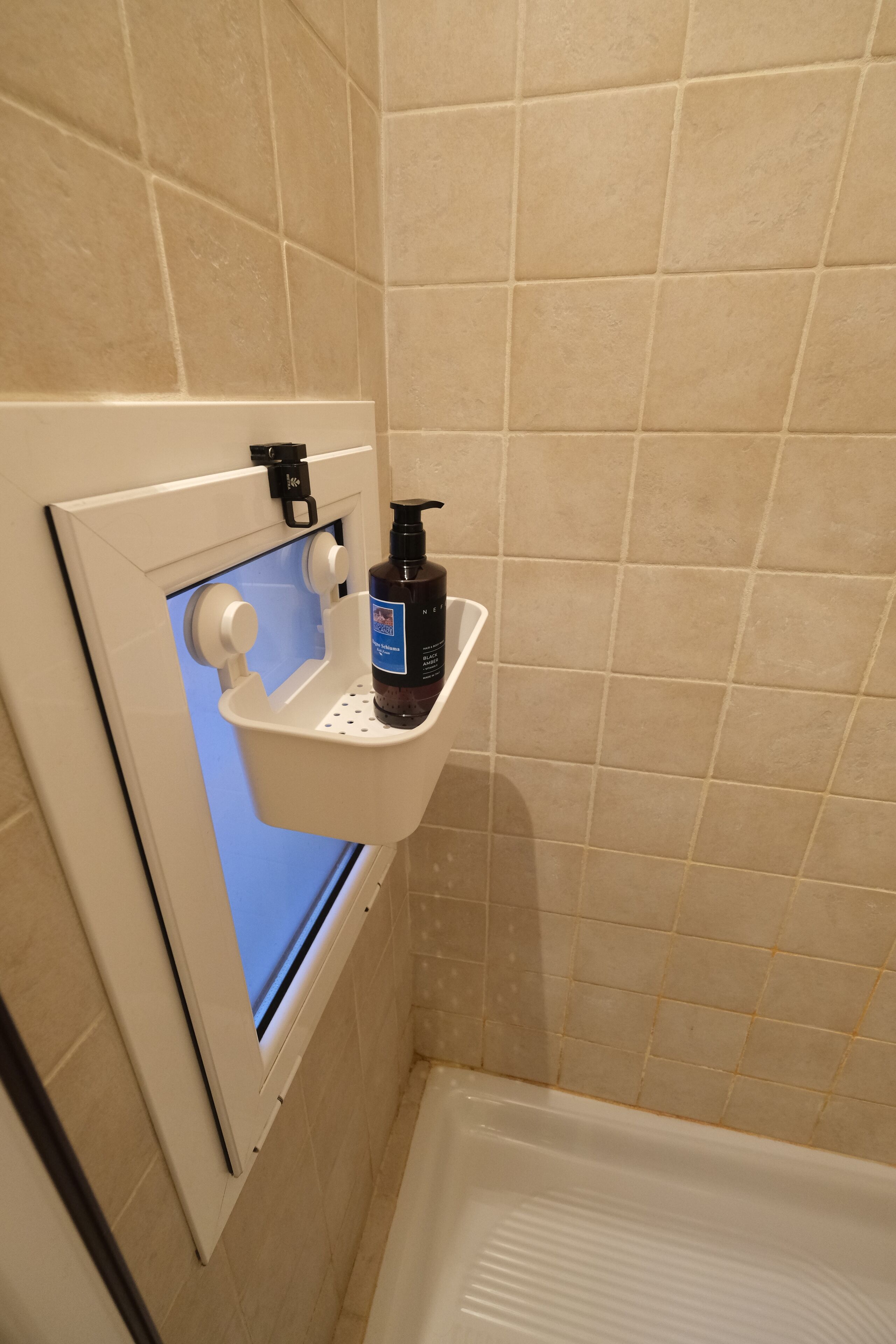 A bathroom with beige tiles, a white sink with a soap dispenser, and a window with a blue tint.
