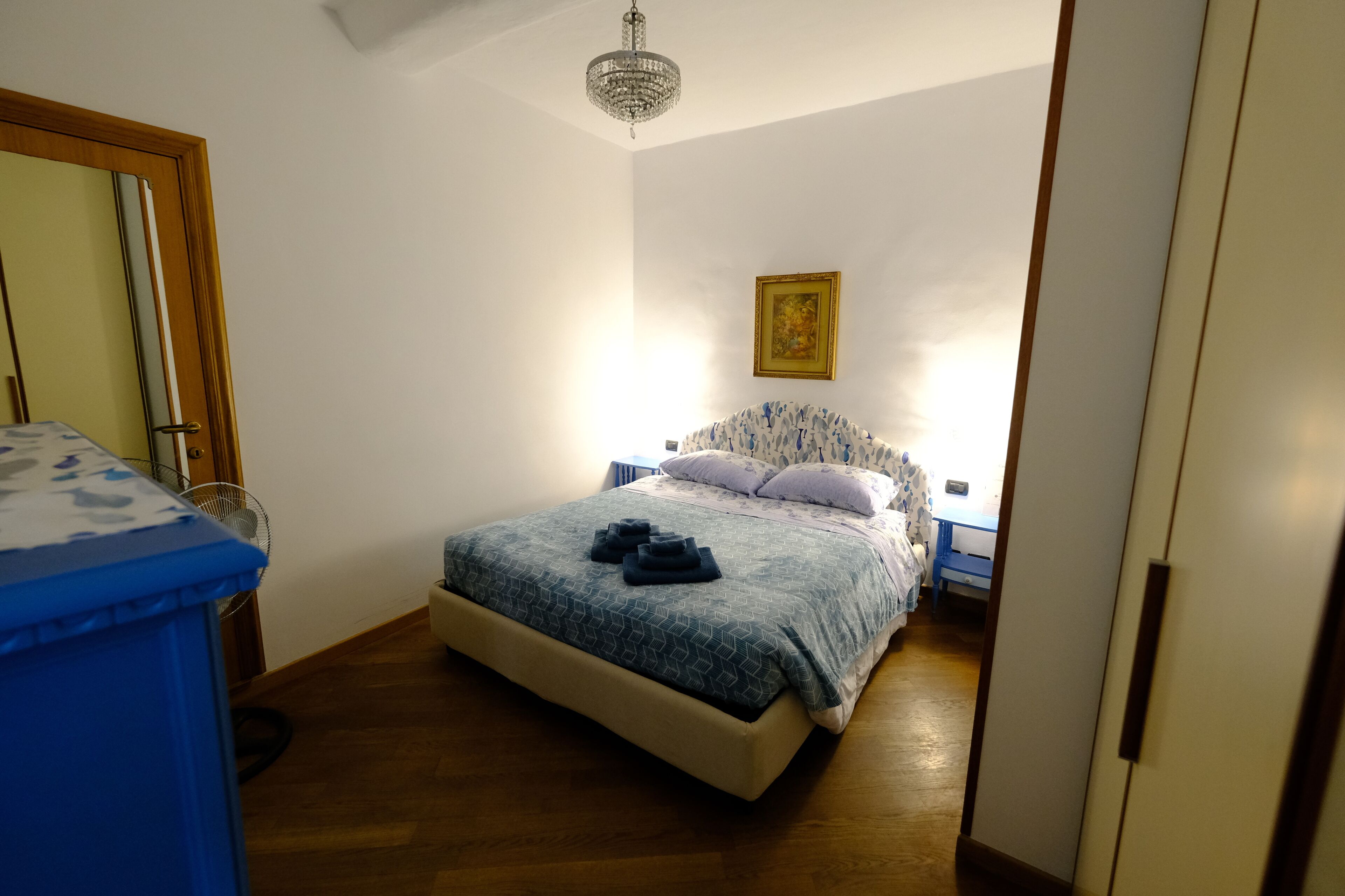 A bedroom with a bed, a dresser, a chandelier, and a painting on the wall.