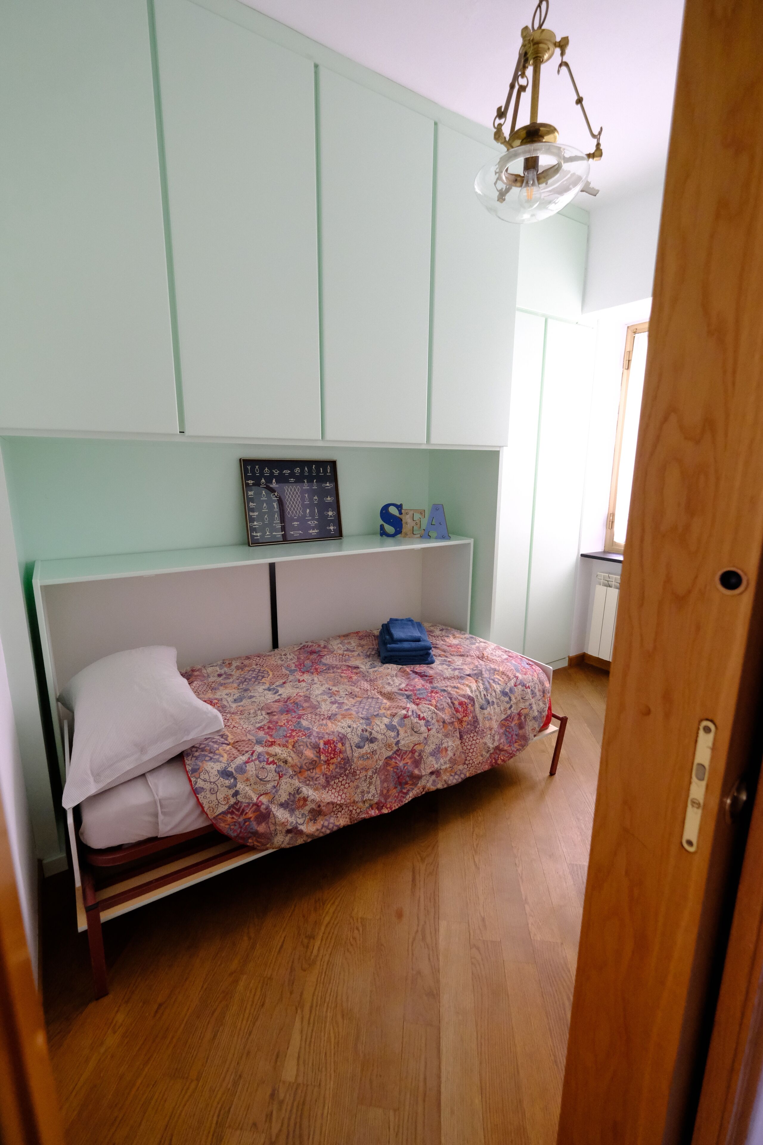 Une petite chambre à coucher avec un lit, une étagère ornée d’objets décoratifs et un luminaire au plafond.