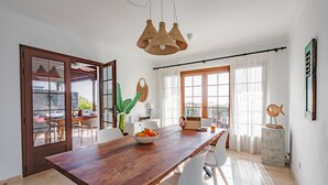 Un comedor con una mesa de madera, sillas blancas, un bol de fruta y una lámpara colgante de fibras naturales.