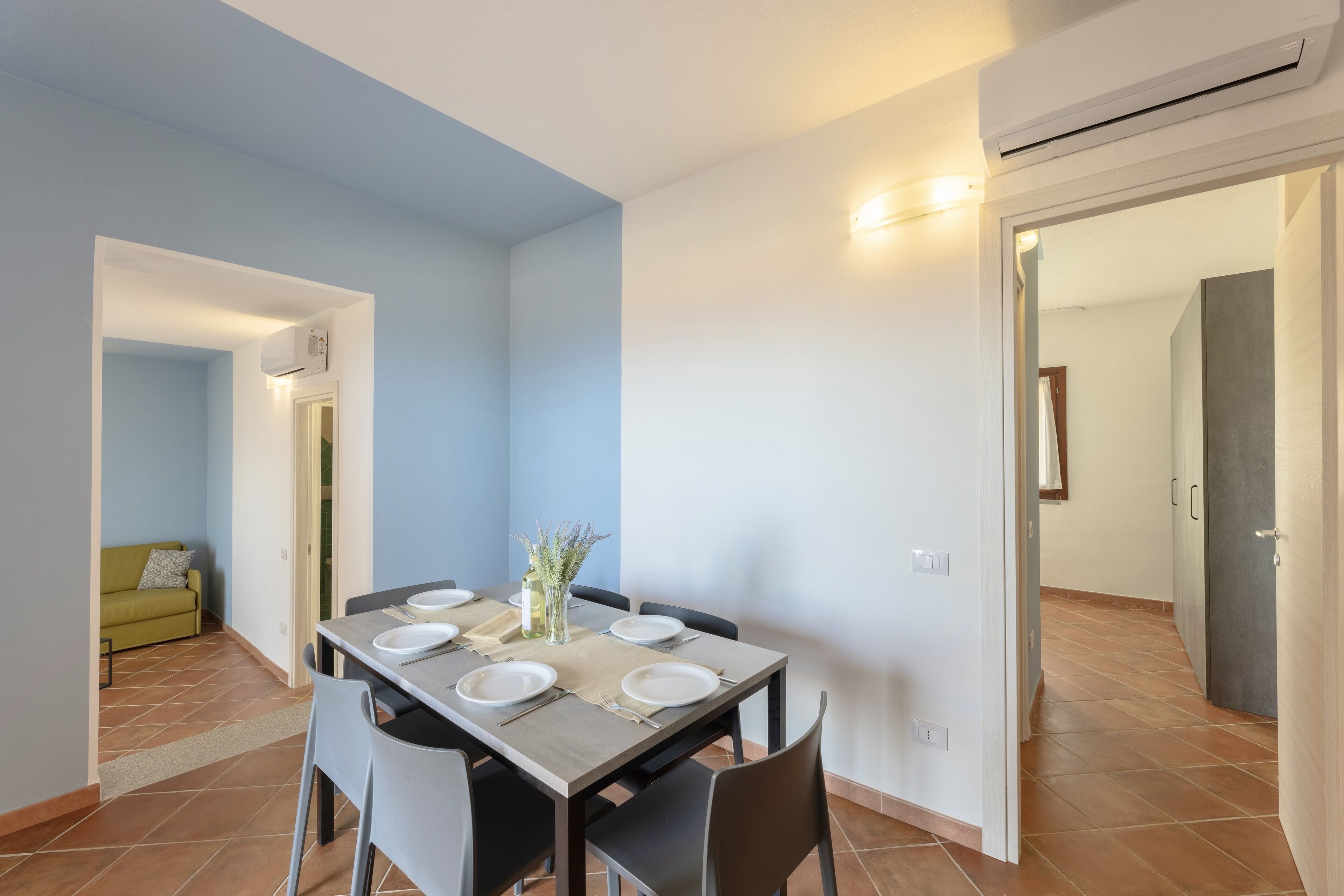A dining area with a table set for four, a sofa, and a door leading to another room.