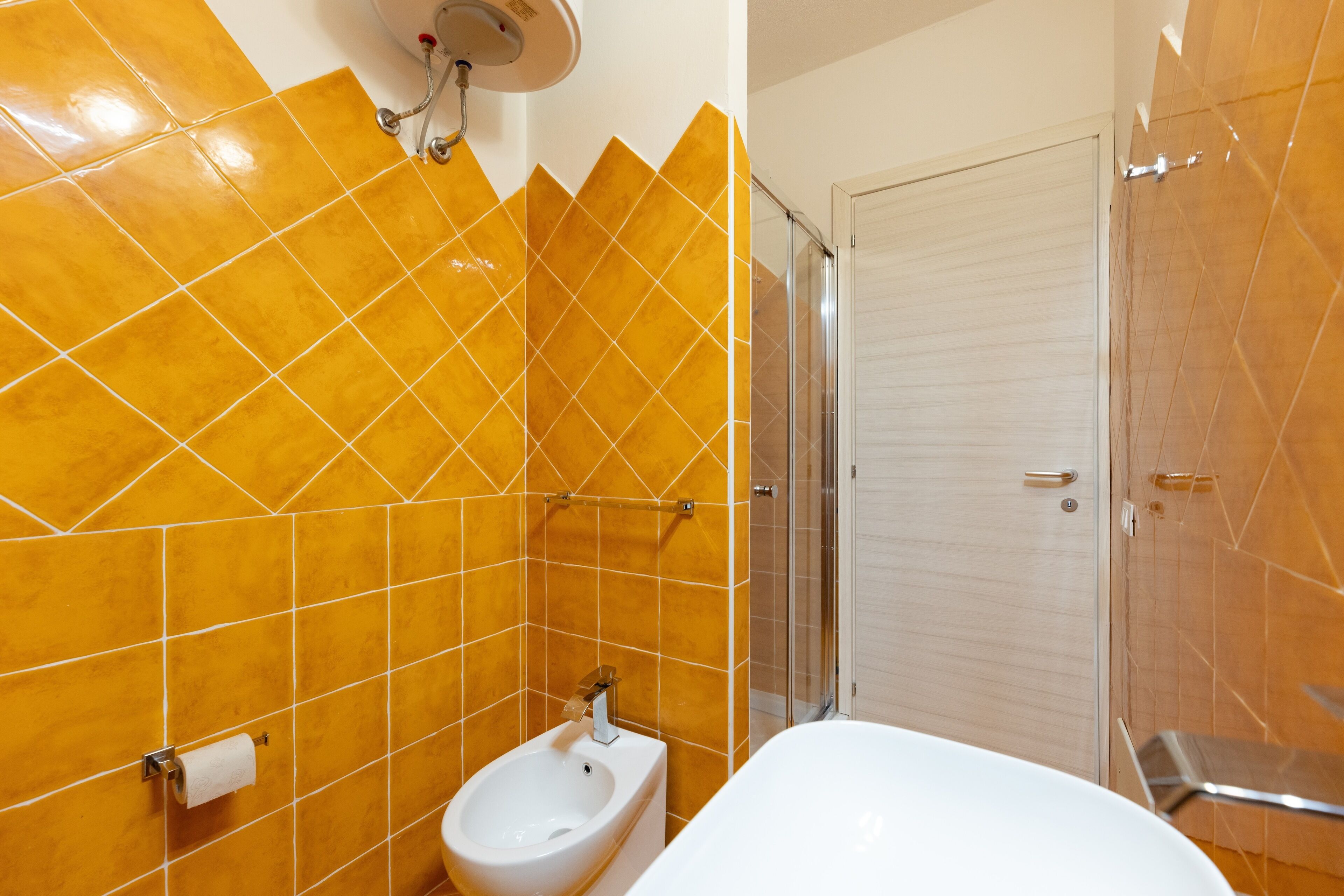 A bathroom with yellow tiles, a bidet, a toilet, and a shower area.