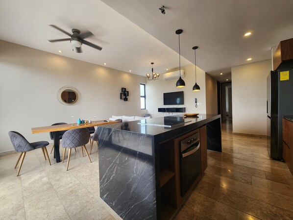 A modern kitchen with a marble island, wooden dining table, and chairs.