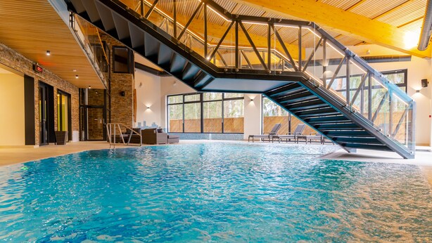 An indoor swimming pool with a glass staircase leading to a balcony. - Spa & Wellness Hotel Fitak (Liptovský Ján)