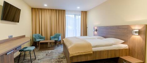 Habitación de hotel con cama, escritorio, dos sillas, televisión y ventana con cortinas.