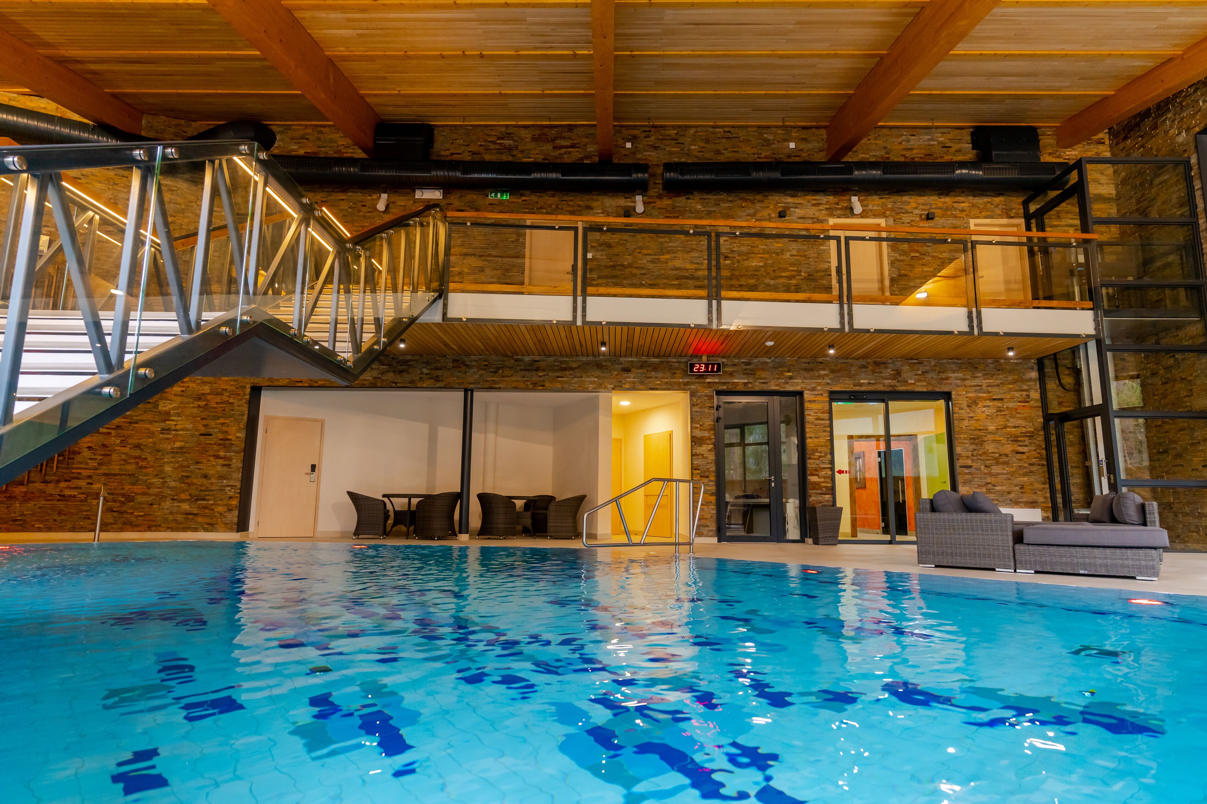 An indoor swimming pool with a glass-walled upper deck, stone walls, and a staircase leading to the upper level.
