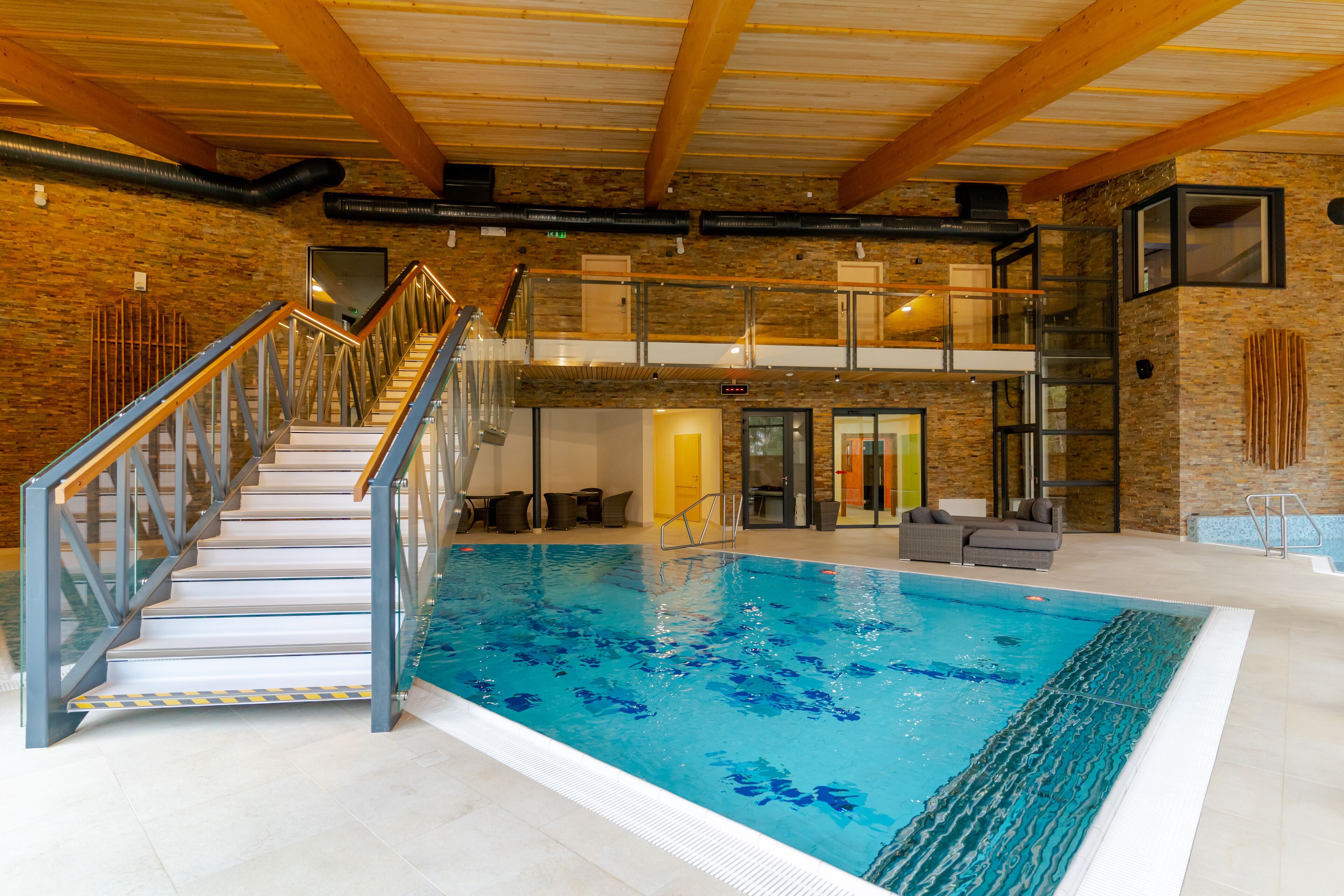 Une piscine intérieure avec un escalier à parois de verre menant à un deuxième niveau.