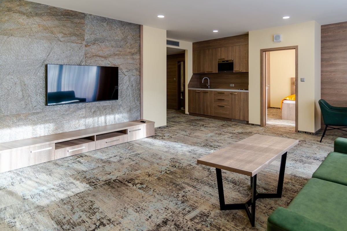 Ein modernes Wohnzimmer mit einem Flachbildfernseher, einem Holztisch und einem grünen Sofa.