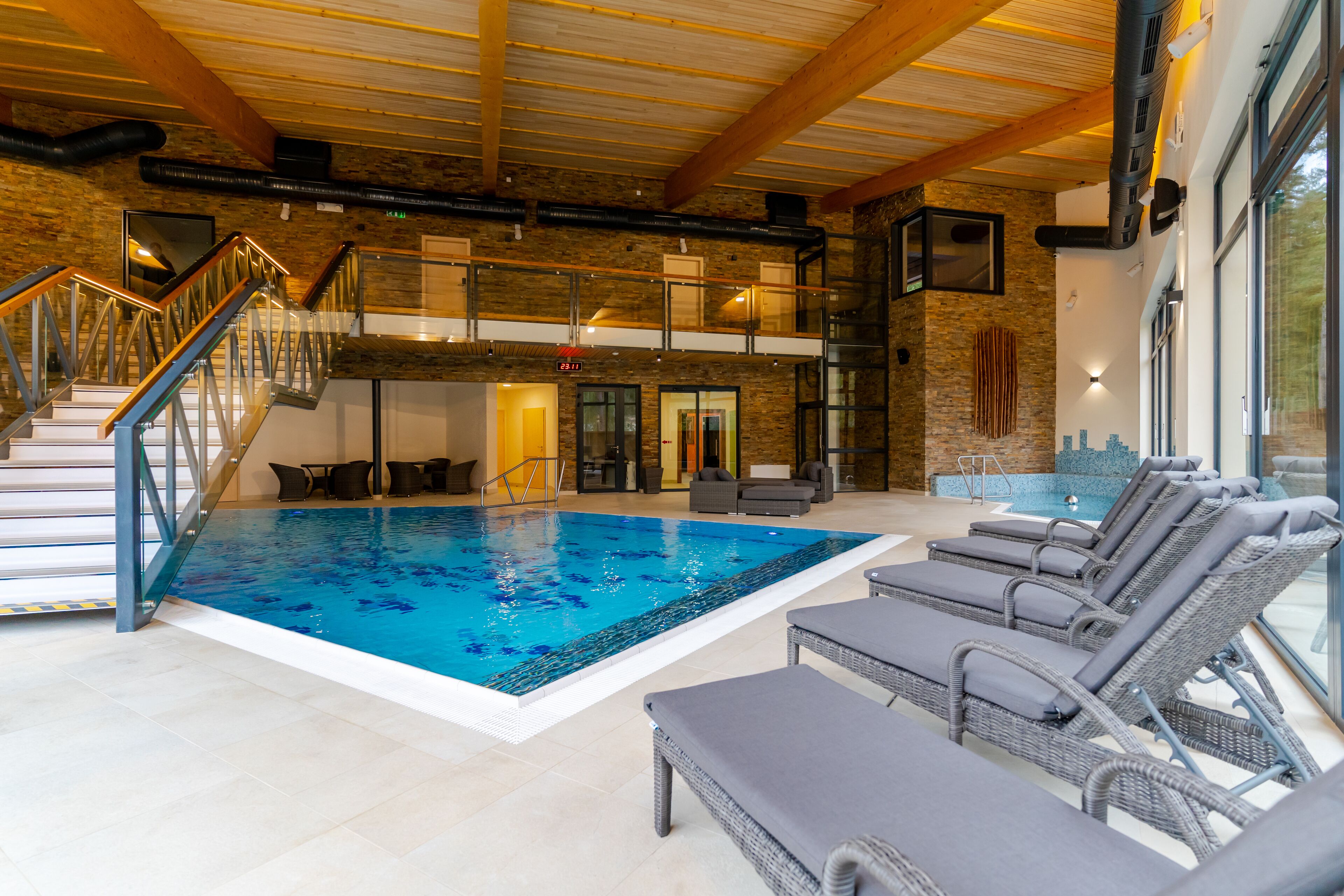 An indoor swimming pool with lounge chairs, a staircase, and a view of the outdoors.