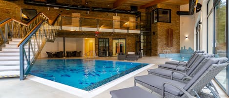 Una piscina interior con sillas de descanso, una escalera y vistas al exterior.