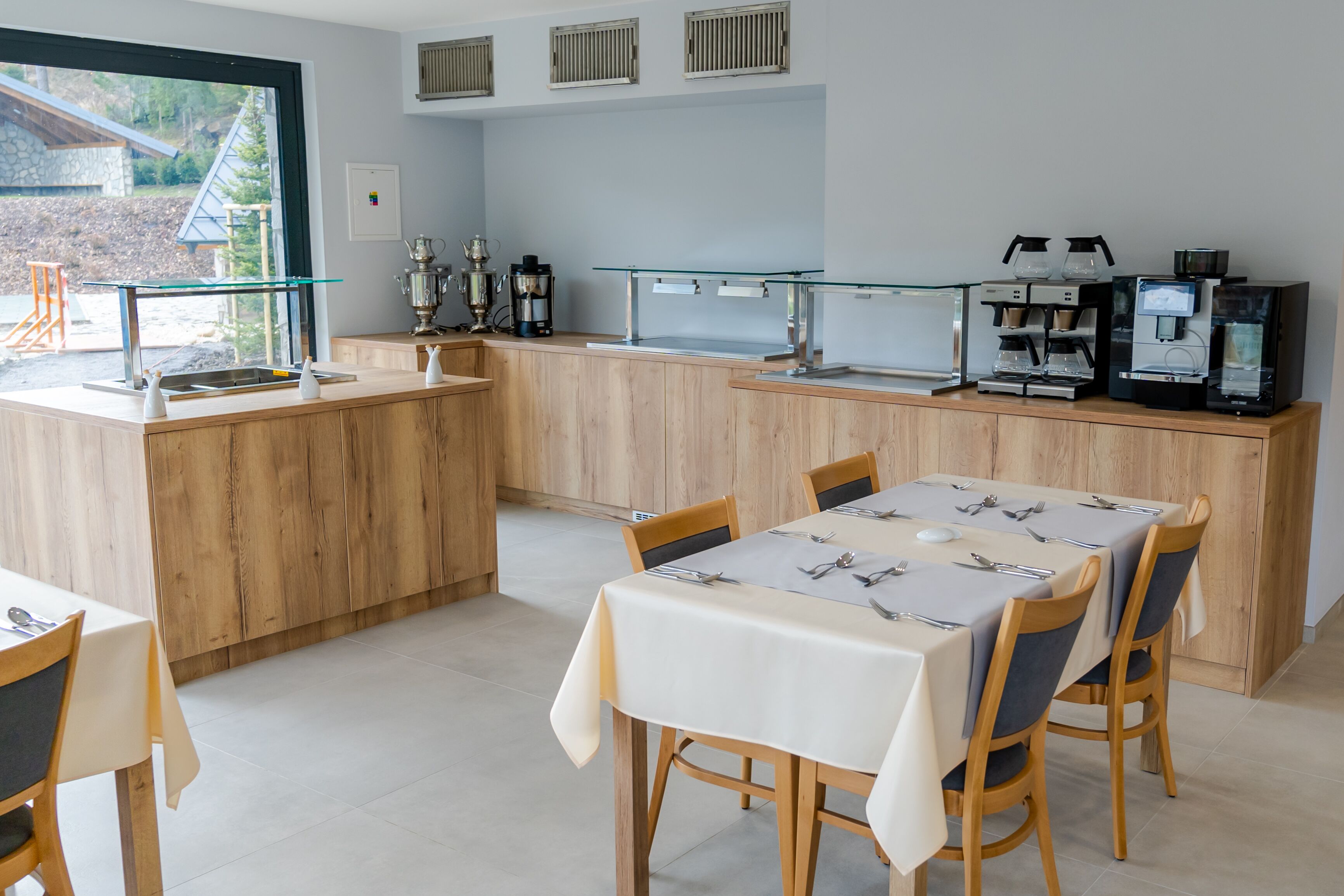 Et moderne køkken med træskabe, en glas kaffestation og et spiseområde med et bord dækket til to.