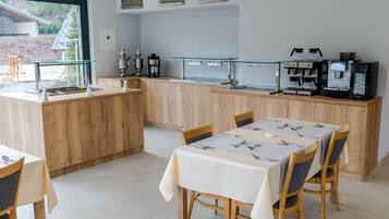 A modern kitchen with wooden cabinets, a glass coffee station, and a dining area with a table set for two.