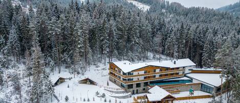 Un moderno albergue con varias habitaciones, piscina y vistas a árboles y montañas nevadas.