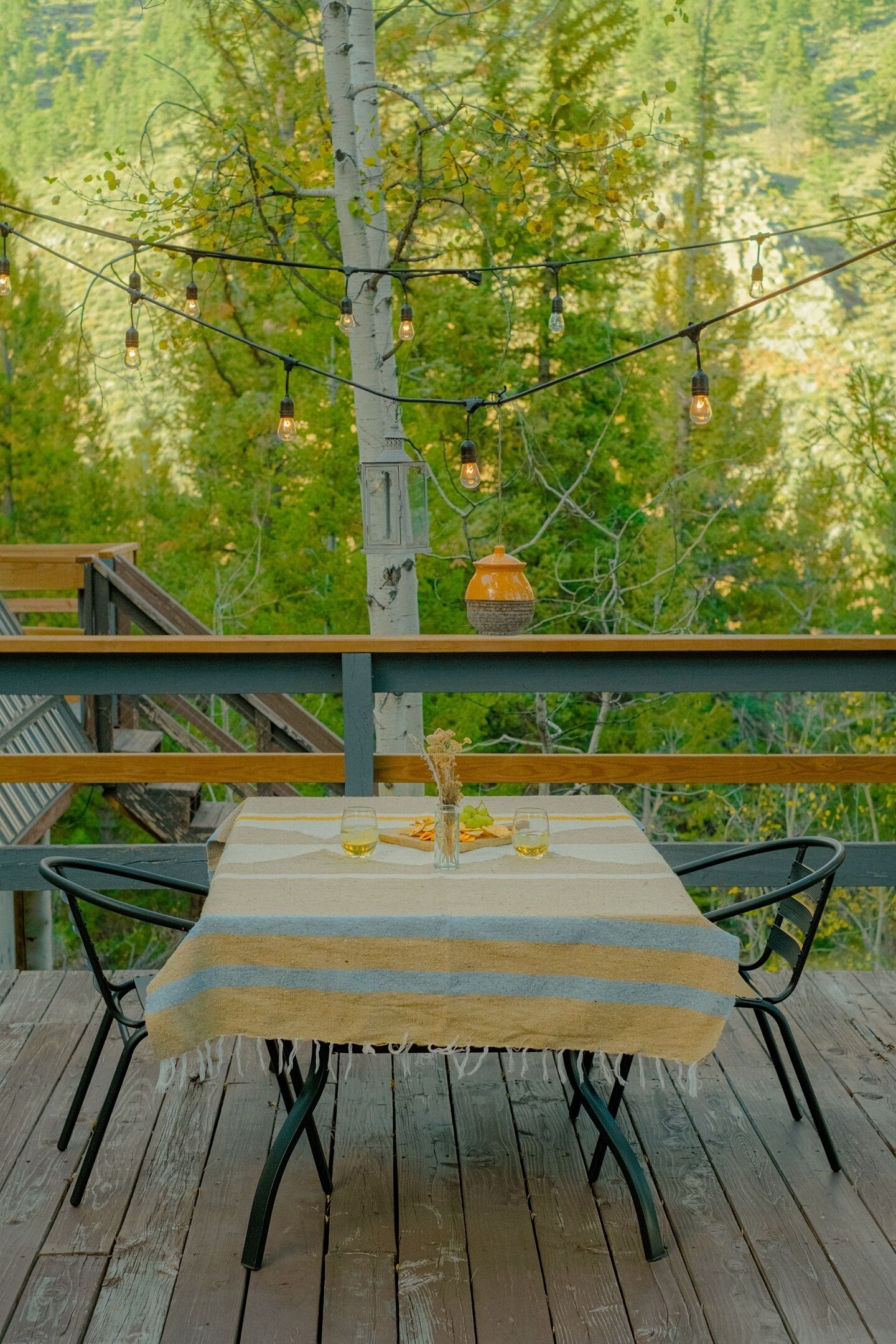 Una terraza de madera con una mesa preparada para dos, rodeada por un bosque.