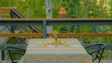 Una terraza de madera con una mesa preparada para dos, rodeada por un bosque.