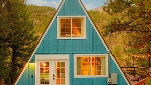 A blue A-frame cabin with a stone-paved entrance, two windows, and a small porch area.