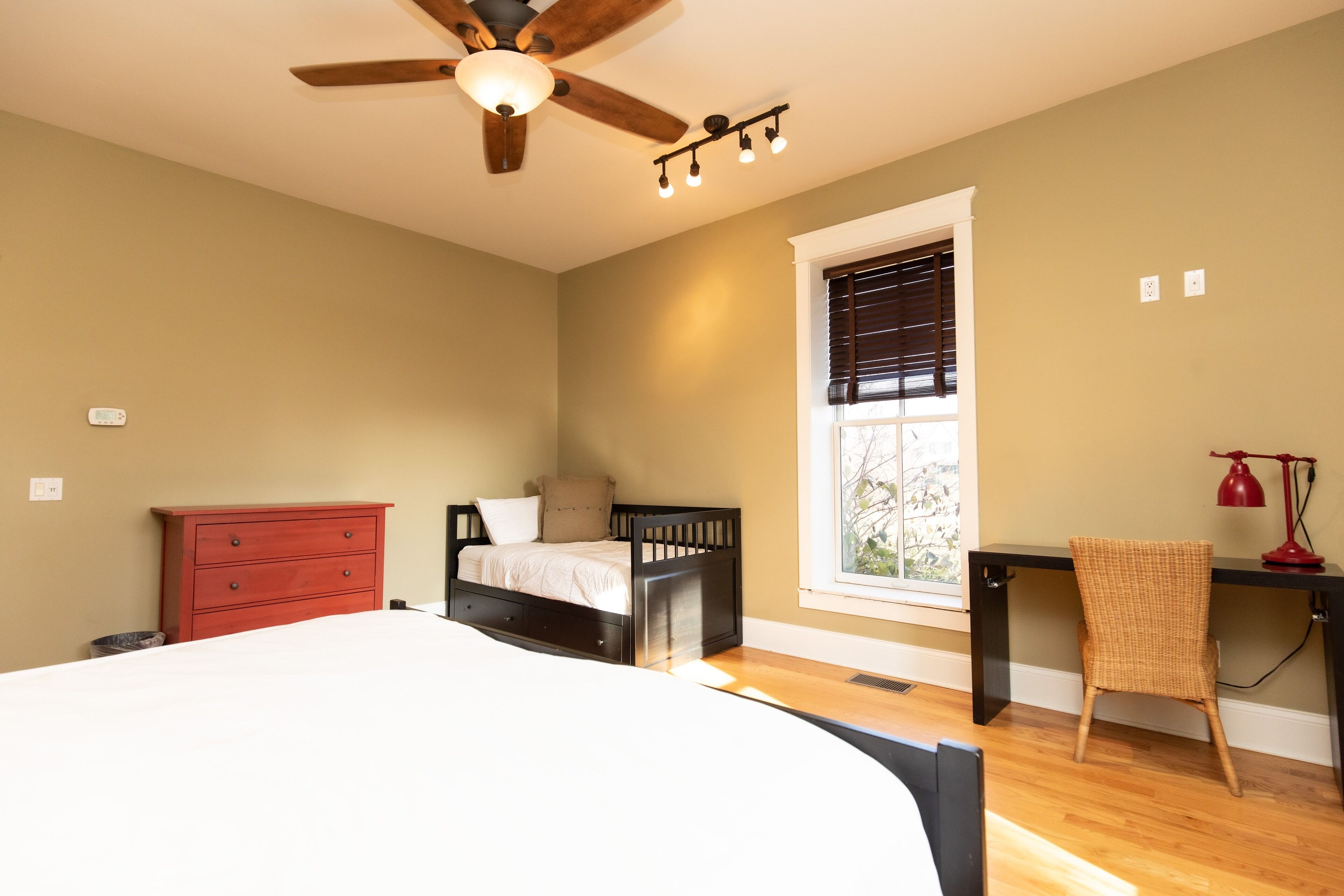 A bedroom with a bed, a desk, a chair, a dresser, and a ceiling fan.