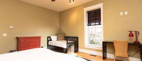 A bedroom with a bed, a desk, a chair, a dresser, and a ceiling fan.