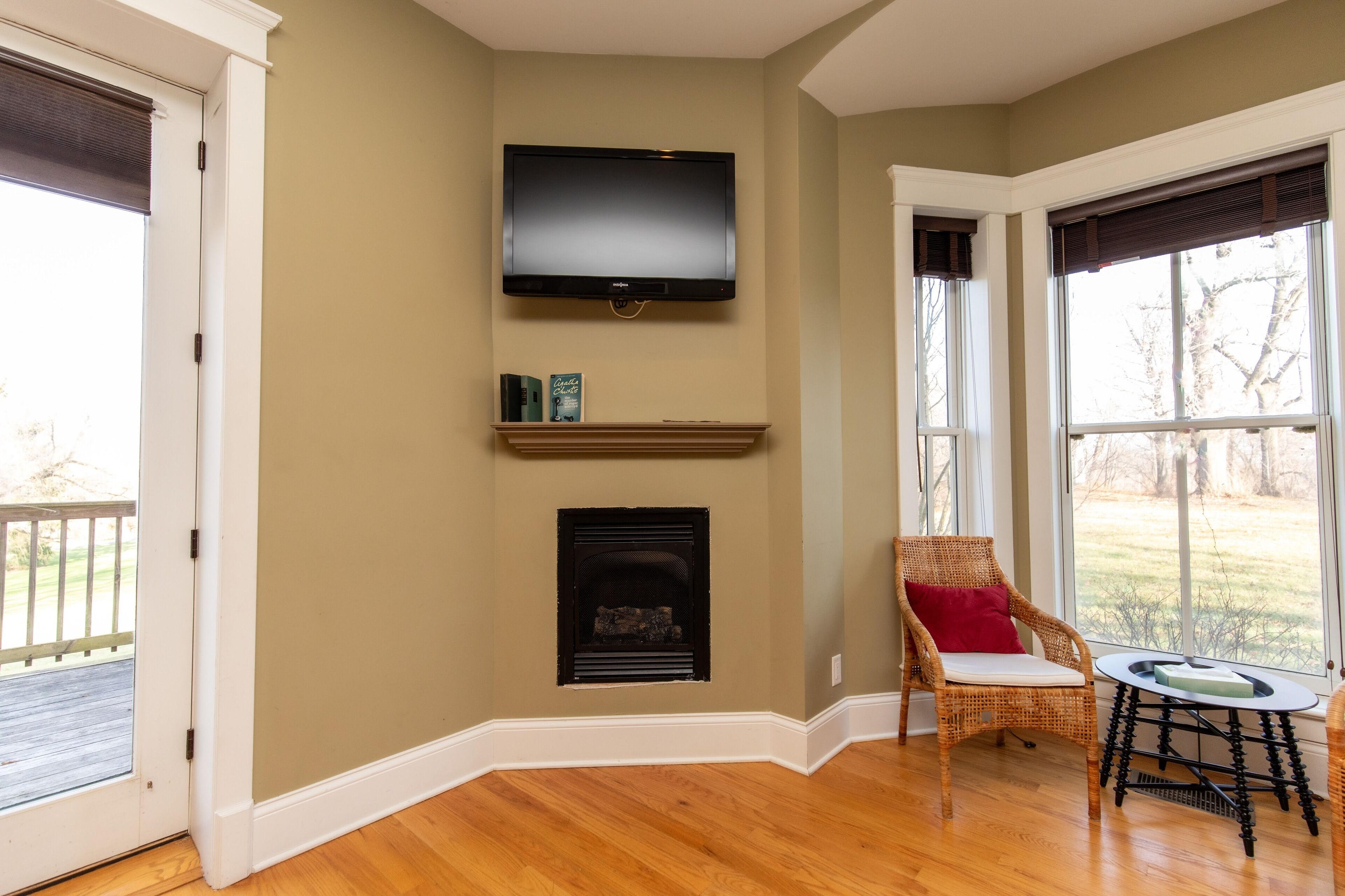 Una habitación con chimenea, televisor montado, sillón de mimbre y vistas al exterior.
