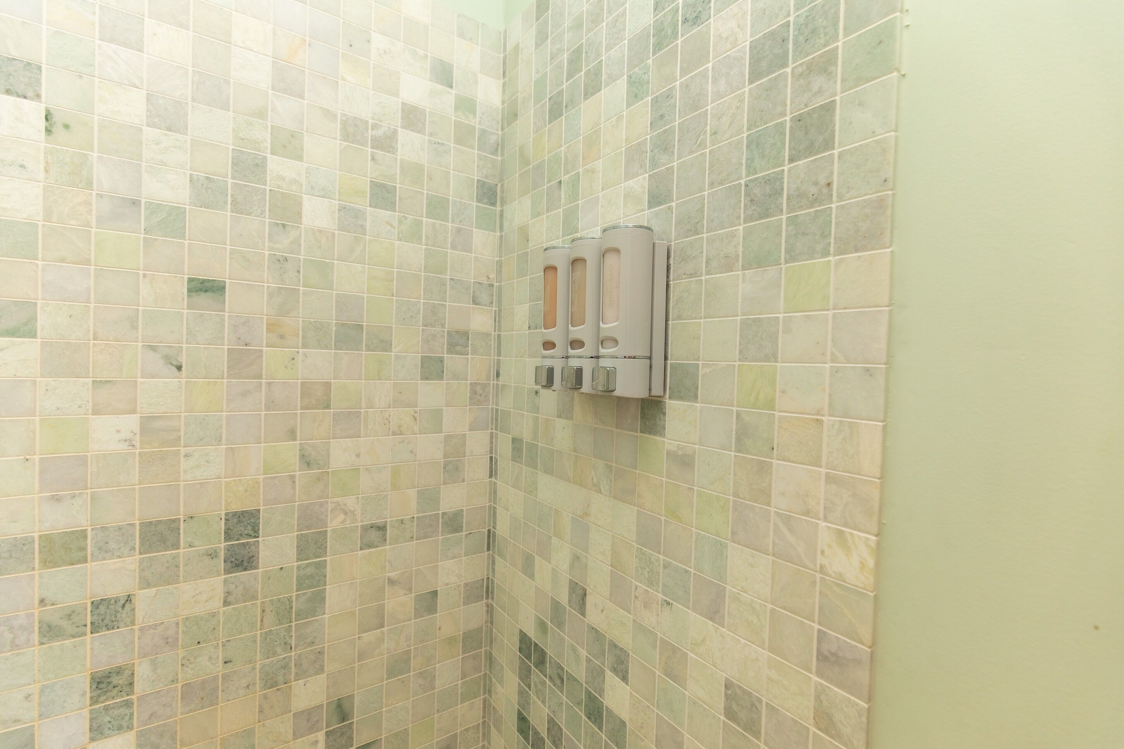 Un baño con pared de azulejos y dispensador de jabón.