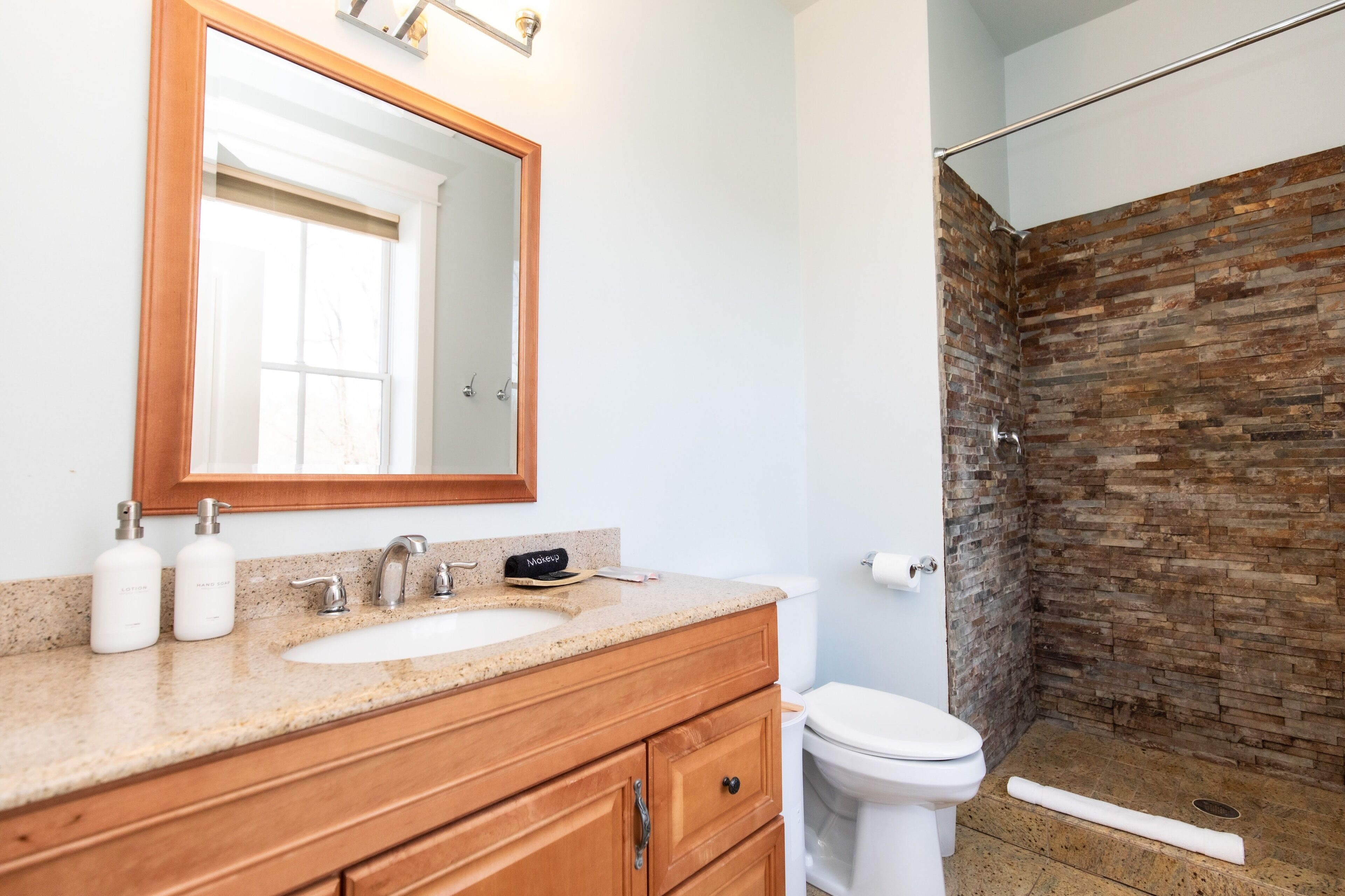 Un baño con tocador de madera, un espejo grande, un lavabo y una ducha con pared de ladrillo.