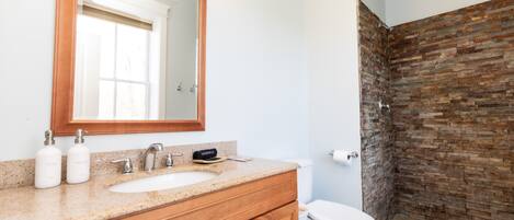 Un baño con tocador de madera, un espejo grande, un lavabo y una ducha con pared de ladrillo.