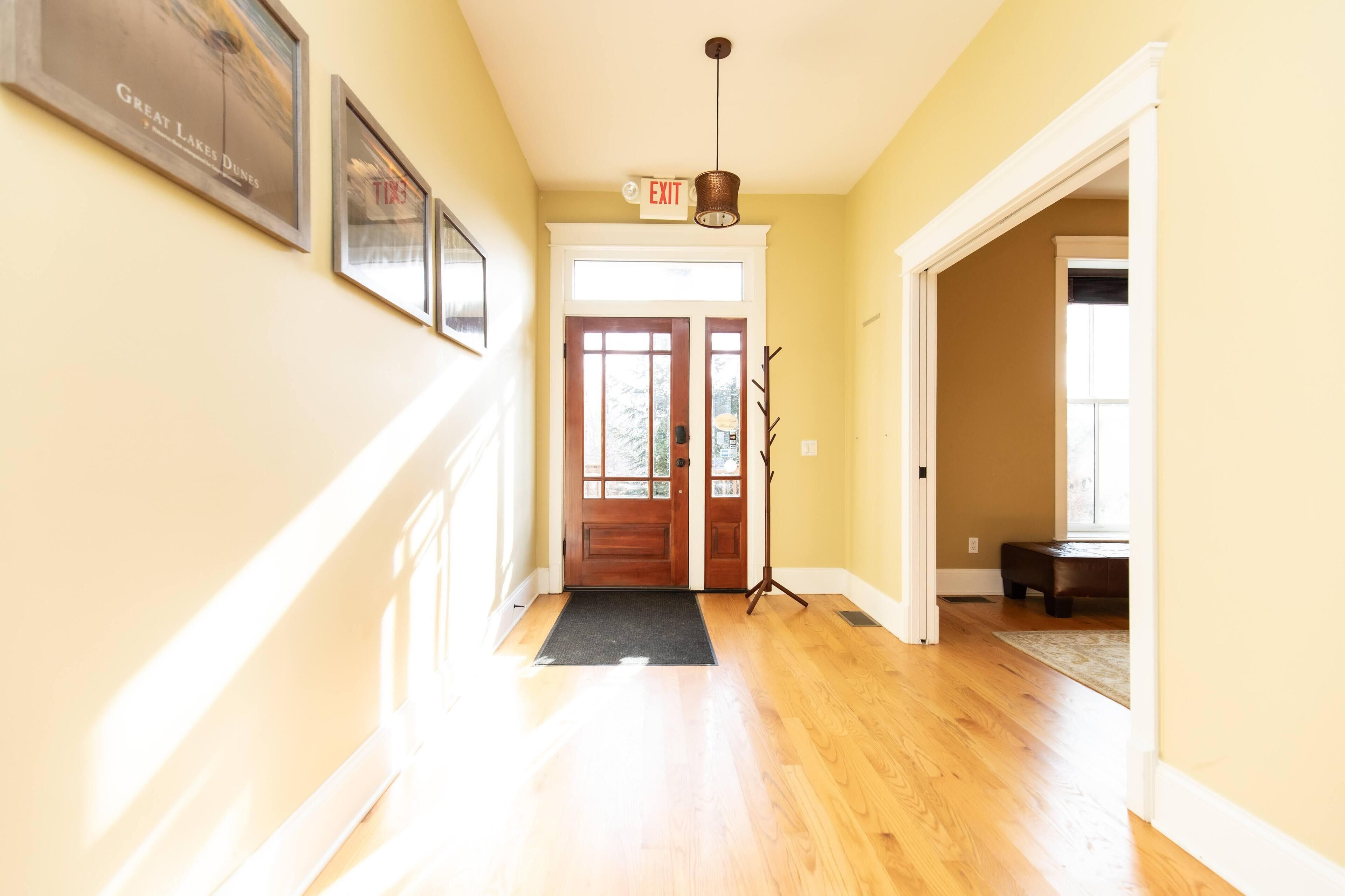 A hallway with wooden floors, a black doormat, a door with glass panels, and a hanging light fixture.