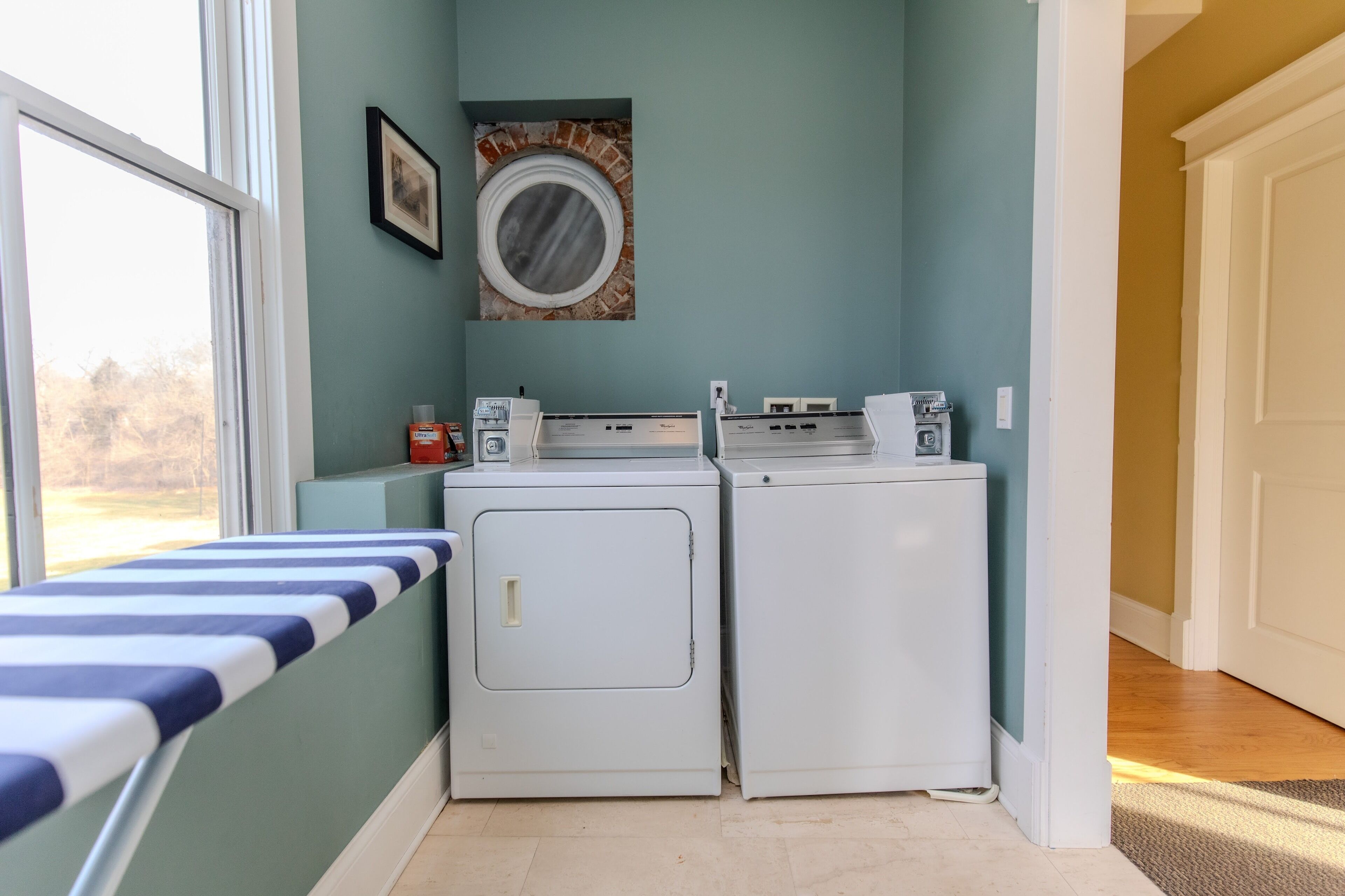 A laundry room with two white washers and dryers, a window, and a door leading to another room.
