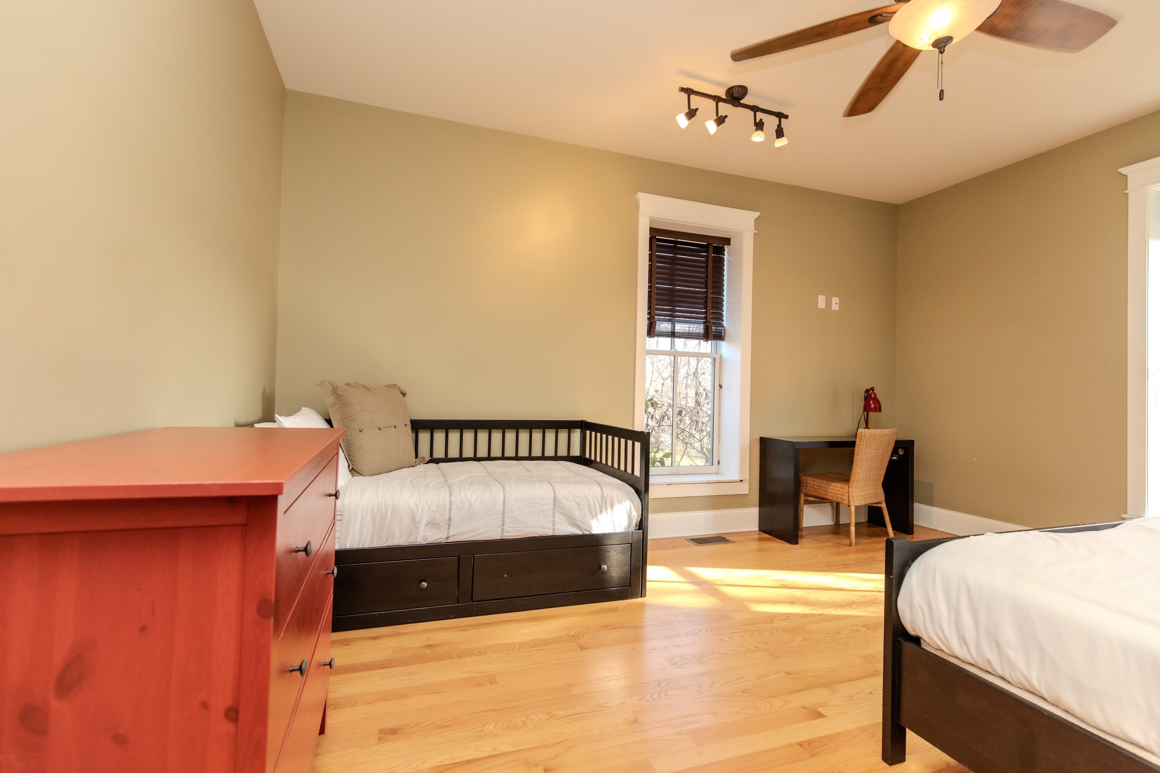 Une chambre à coucher comprenant un lit, un bureau, une chaise, une commode et une fenêtre avec des stores.