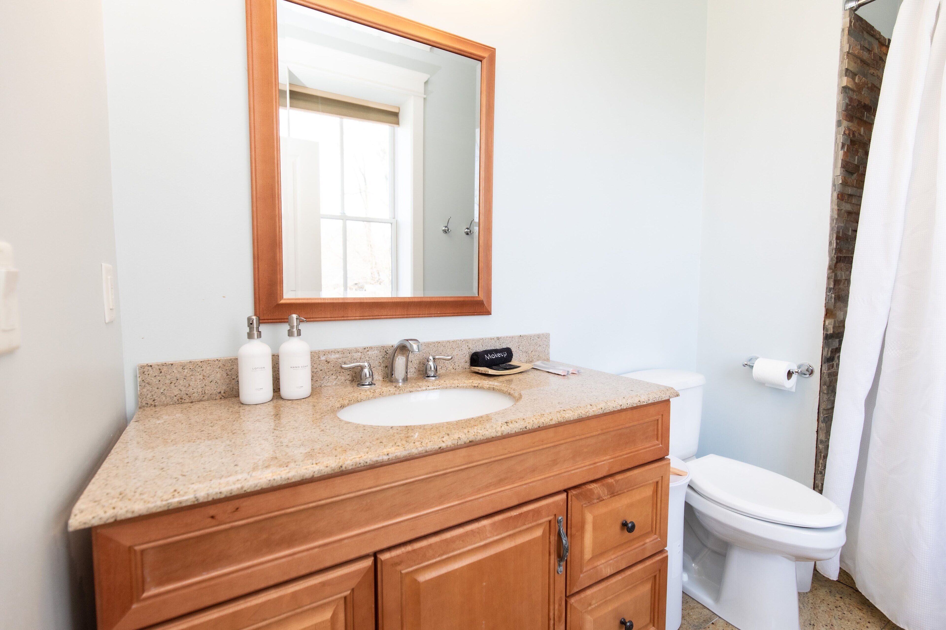 A bathroom with a wooden vanity, a sink, a mirror, a toilet, and a shower curtain.