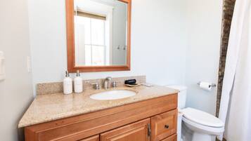 A bathroom with a wooden vanity, a sink, a mirror, a toilet, and a shower curtain.
