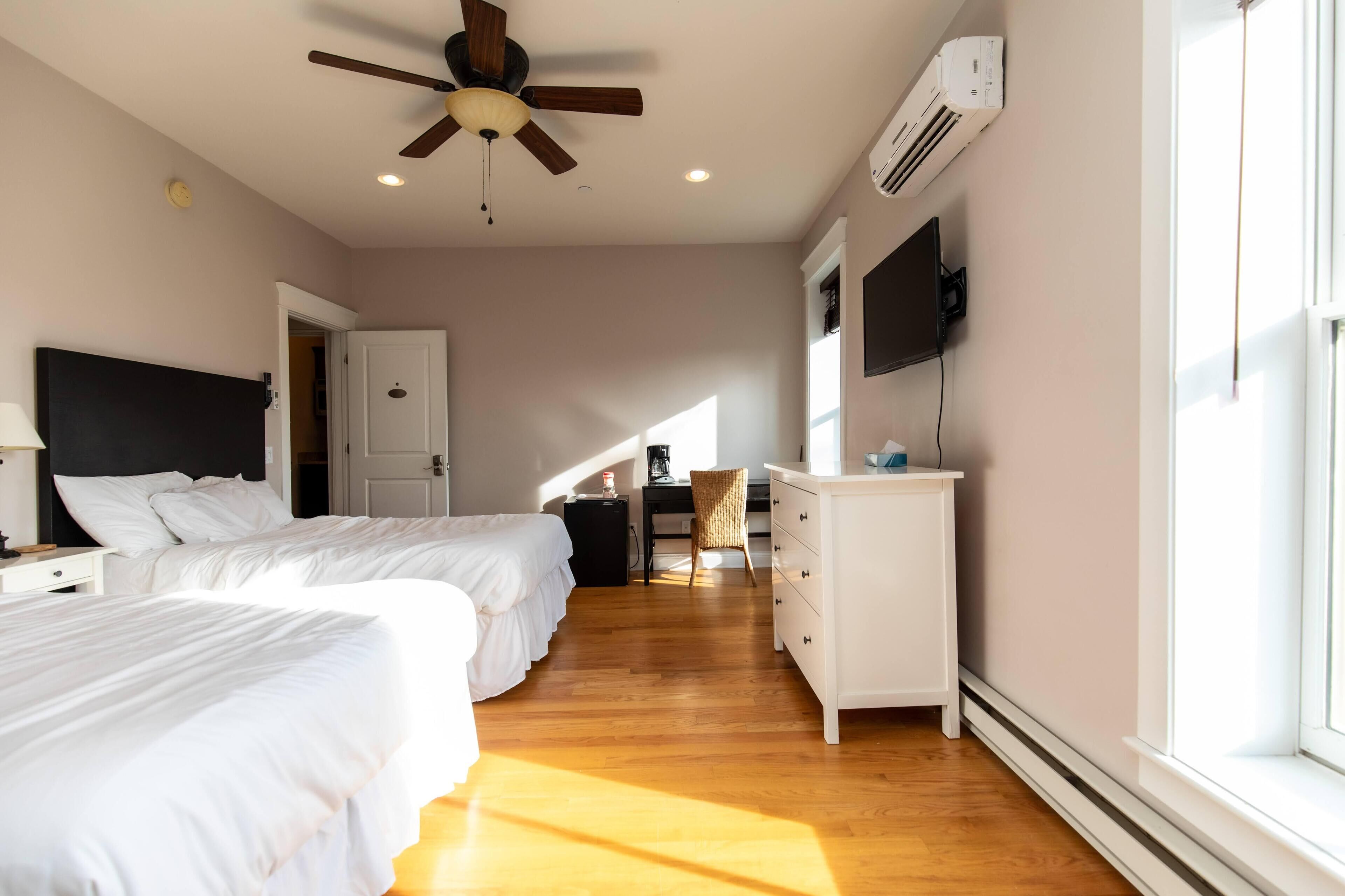 A bedroom with two beds, a desk, a chair, a ceiling fan, and a TV.