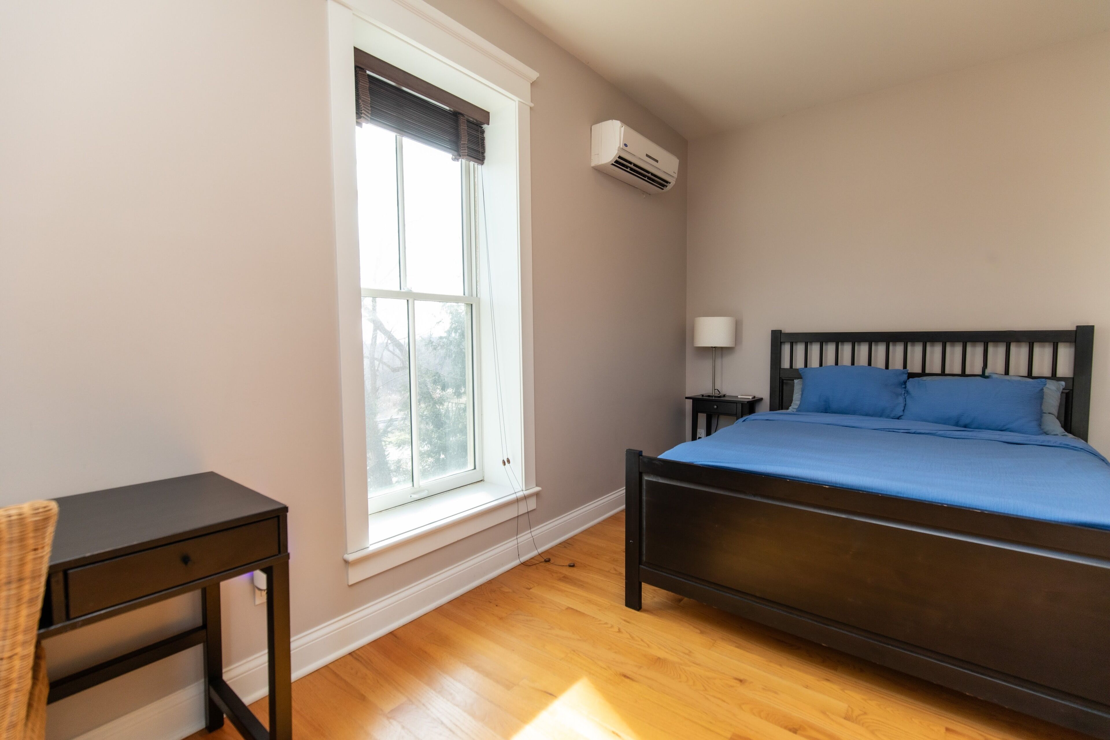 Un dormitorio con cama, escritorio, ventana y aire acondicionado.