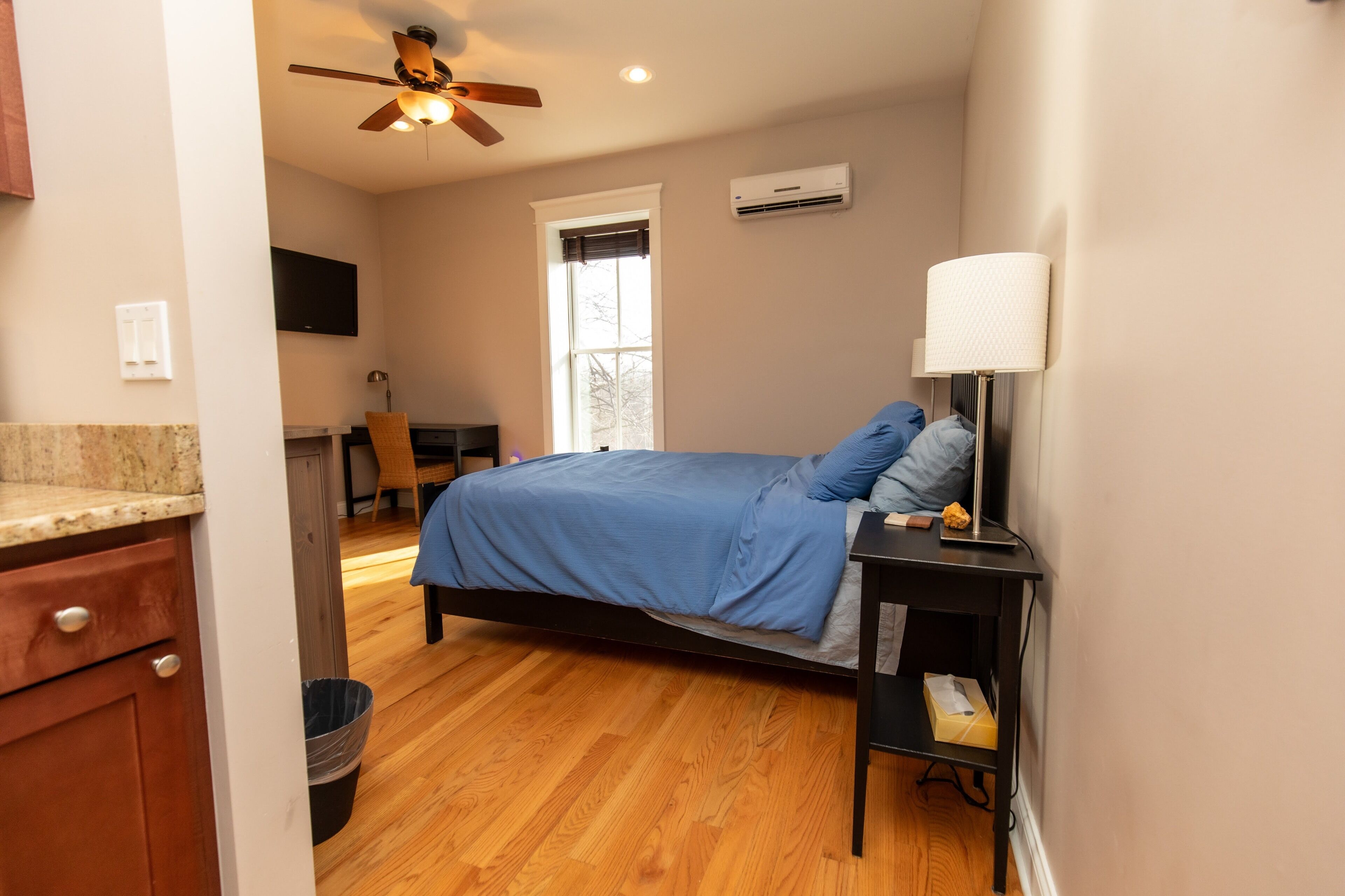 Un dormitorio con cama, escritorio, silla, lámpara y ventilador de techo.