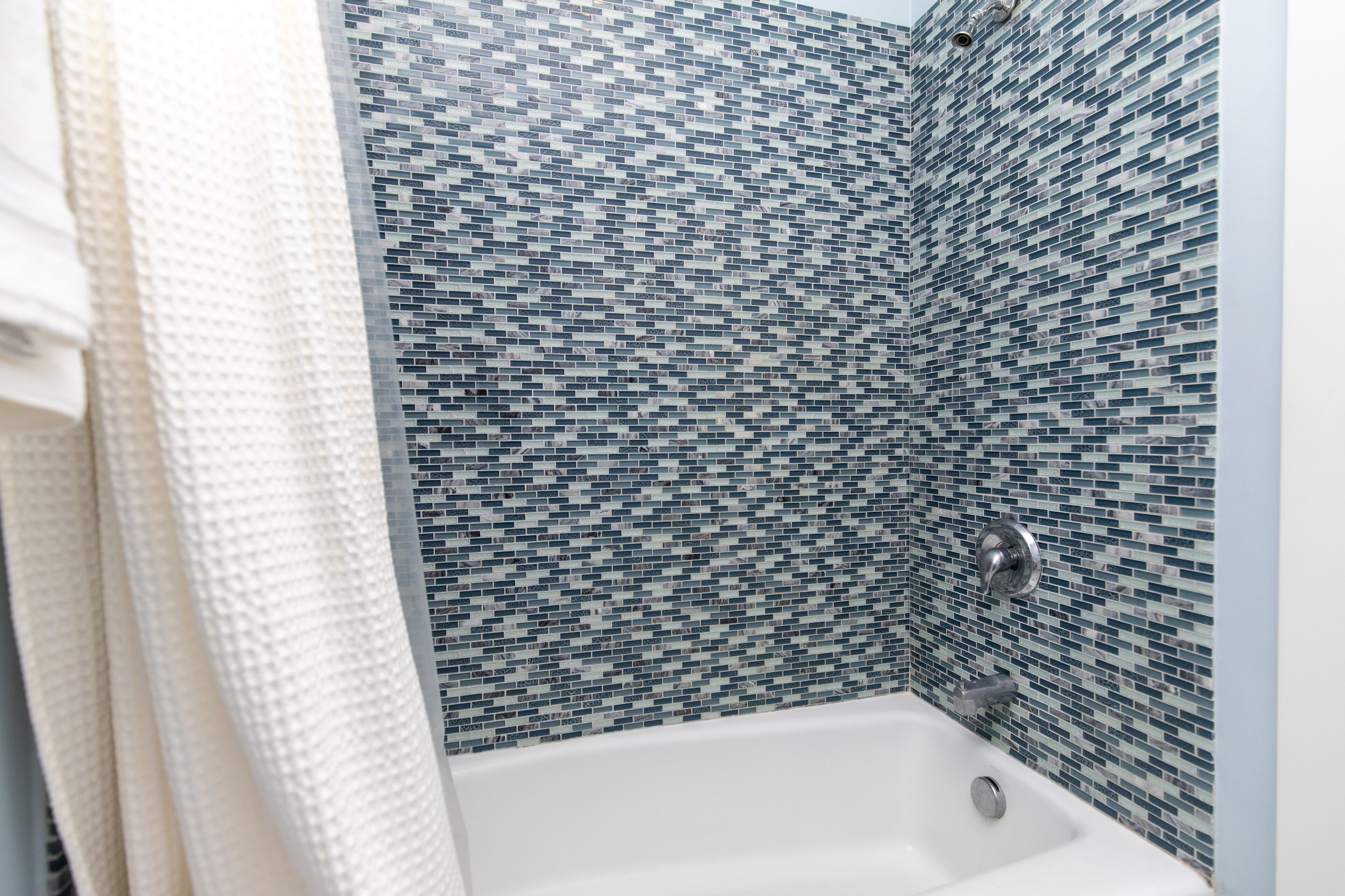 A bathroom with a white bathtub and a mosaic tile wall.