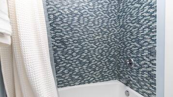 A bathroom with a white bathtub and a mosaic tile wall.