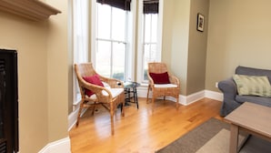 A living room with two wicker chairs, a small table, and a grey sofa. - Furness Mansion (Chesterton)