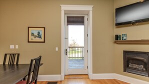 A dining area with a table and chairs, a door leading to a balcony, a fireplace, and a mounted television. - Furness Mansion (Chesterton)