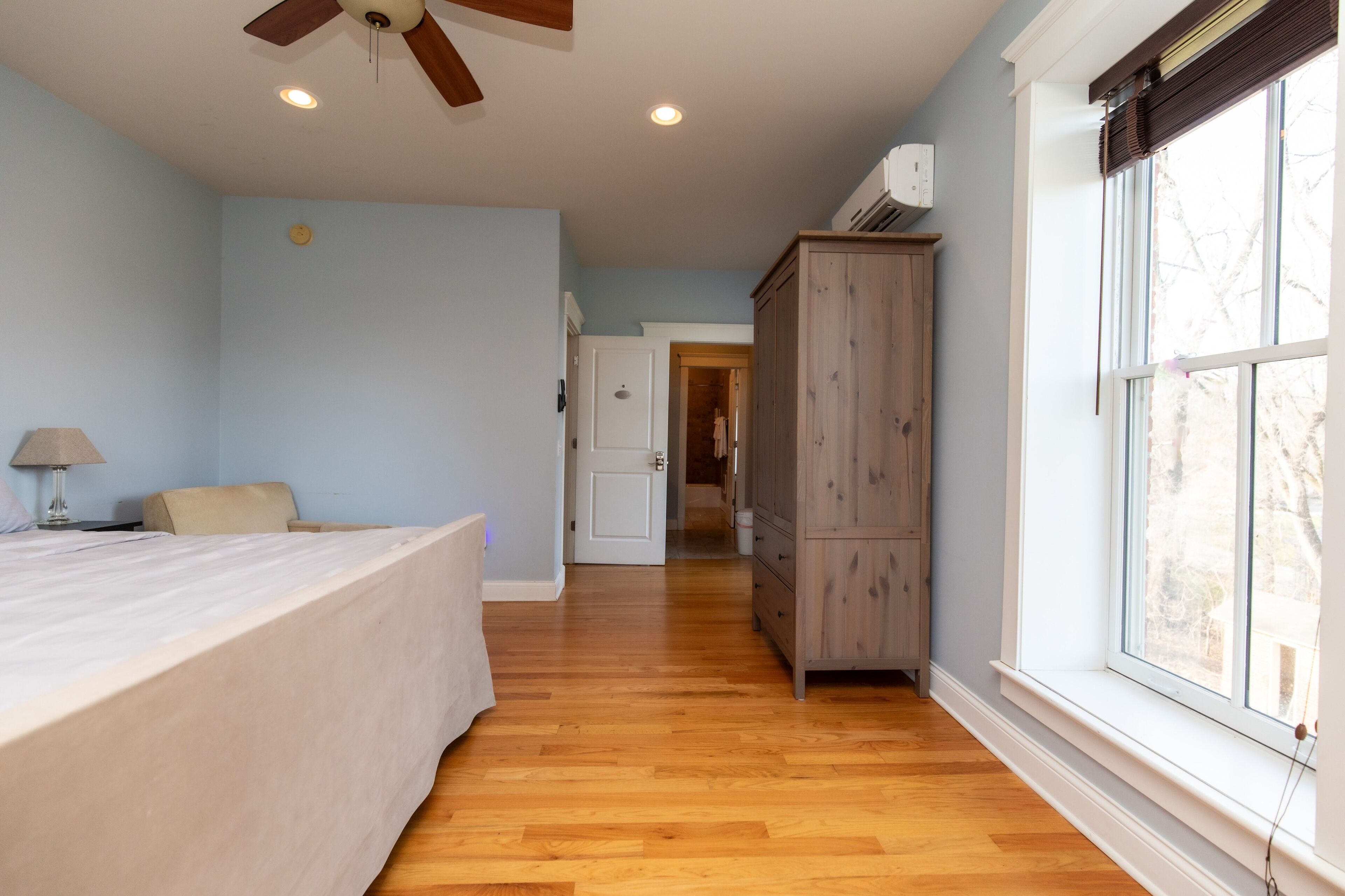 Une chambre à coucher comprenant un lit, une table de chevet, un ventilateur de plafond et une fenêtre avec des stores.