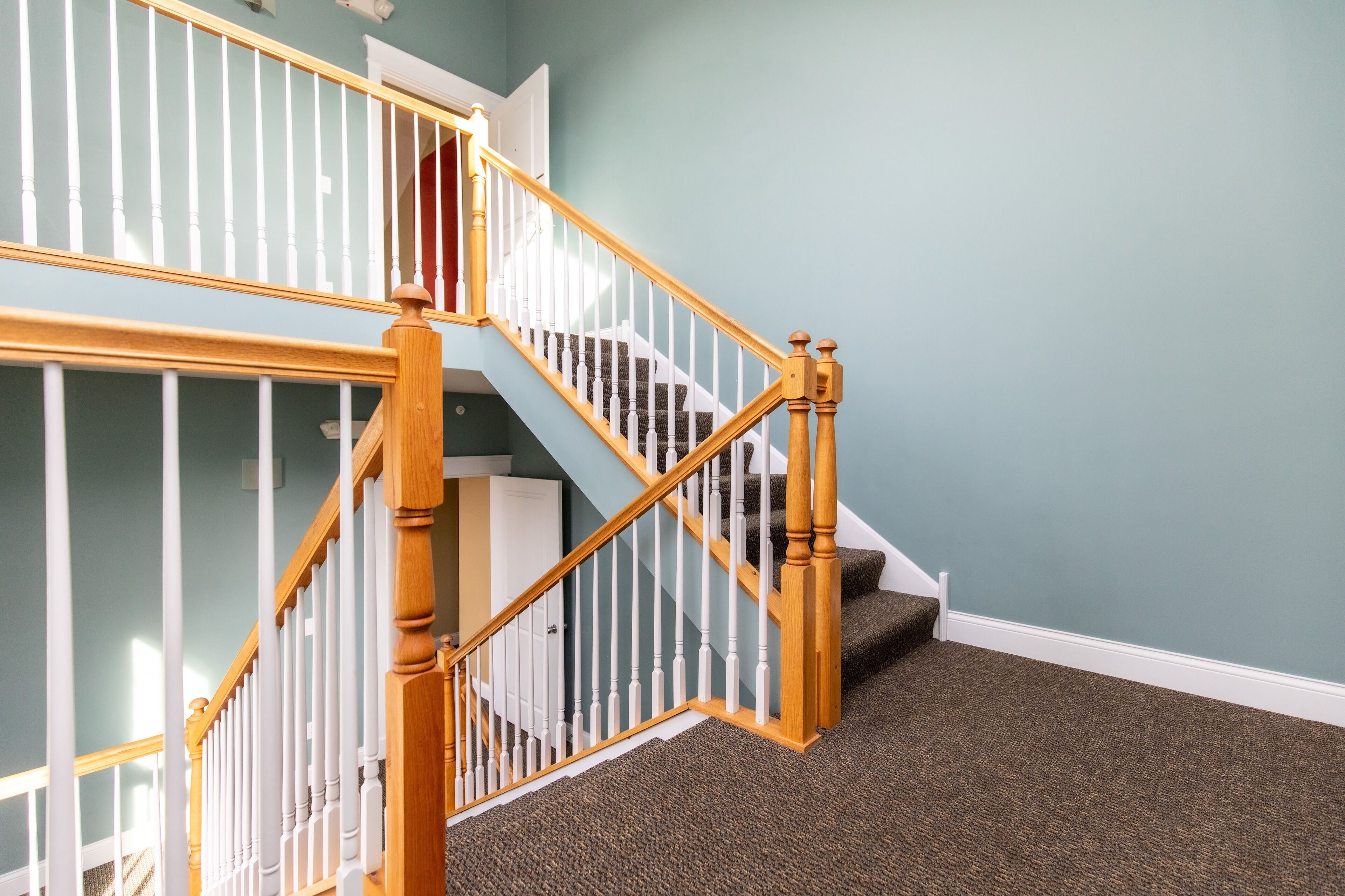 Una escalera con balaustres de madera y barandillas blancas, escalones alfombrados y una pared color aguamarina.