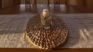 Ein Esstisch mit einer gewebten Tischmatte, zwei Stühlen und einem Glas mit Kerze.