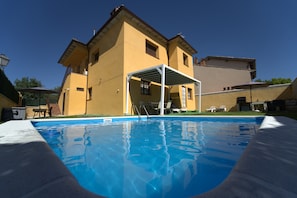 A swimming pool with a covered patio area, a yellow building, and a clear blue sky.